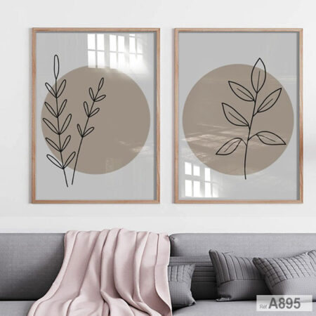 Deux cadres muraux beiges et gris de style boho-botanique avec des illustrations minimalistes de branches de plantes noires, sur un mur au-dessus d'un canapé gris avec un plaid rose.